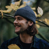 Model met muts glimlacht opzij en draagt een oorsteker met een kubus