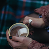 Model draagt zilveren zegelring om duim en houdt een emaillemok met warme chocolademelk en een marshmallow vast